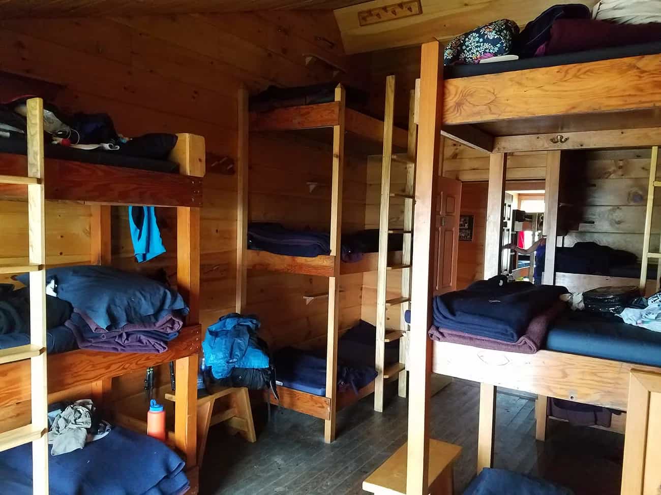 Bunk beds with bedding and gear inside a wooden Galehead Hut interior.