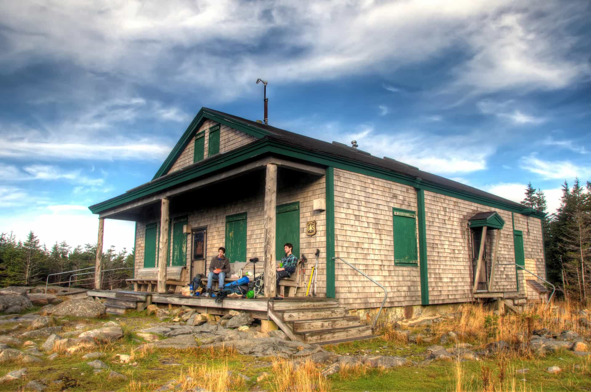 Galehead Hut with hikers resting on the porch under a dramatic cloudy sky.