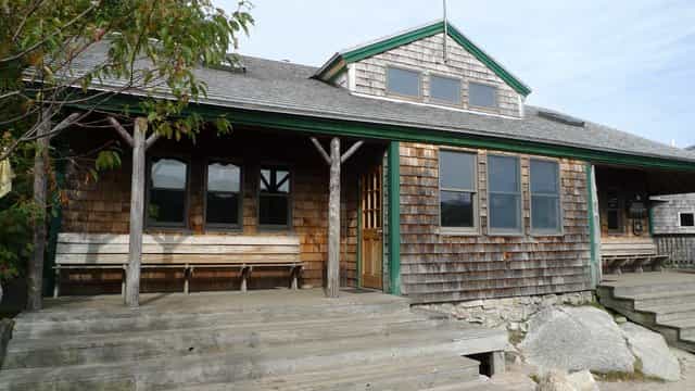 Zealand Falls Hut with weathered wood shingles, green trim, and wooden porch benches.