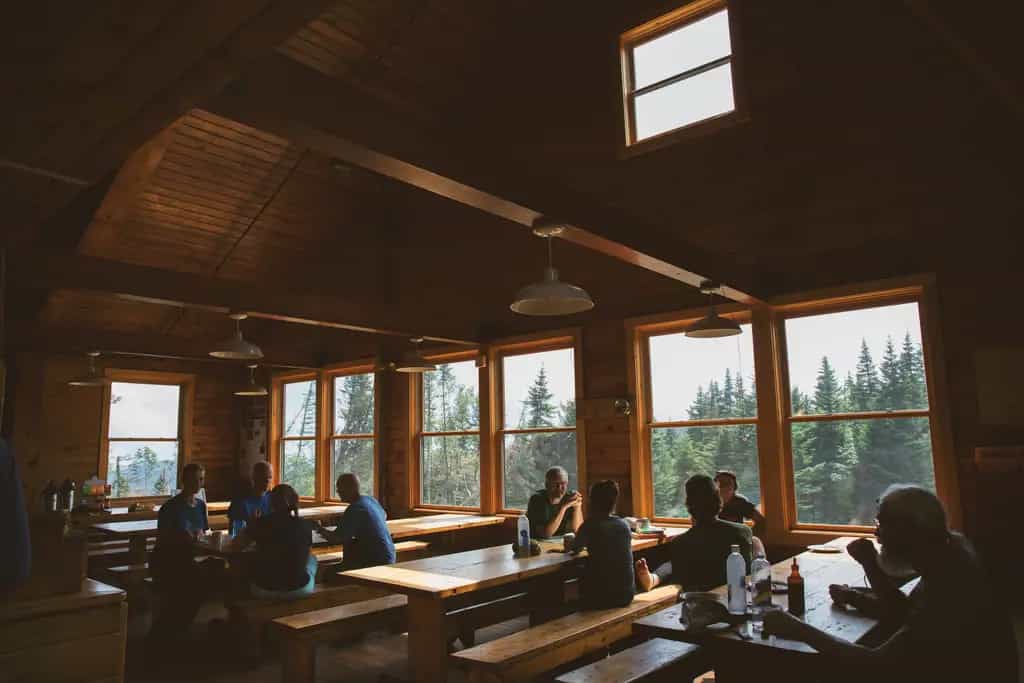 Hikers dining inside Mizpah Spring Hut with views of evergreen forest outside