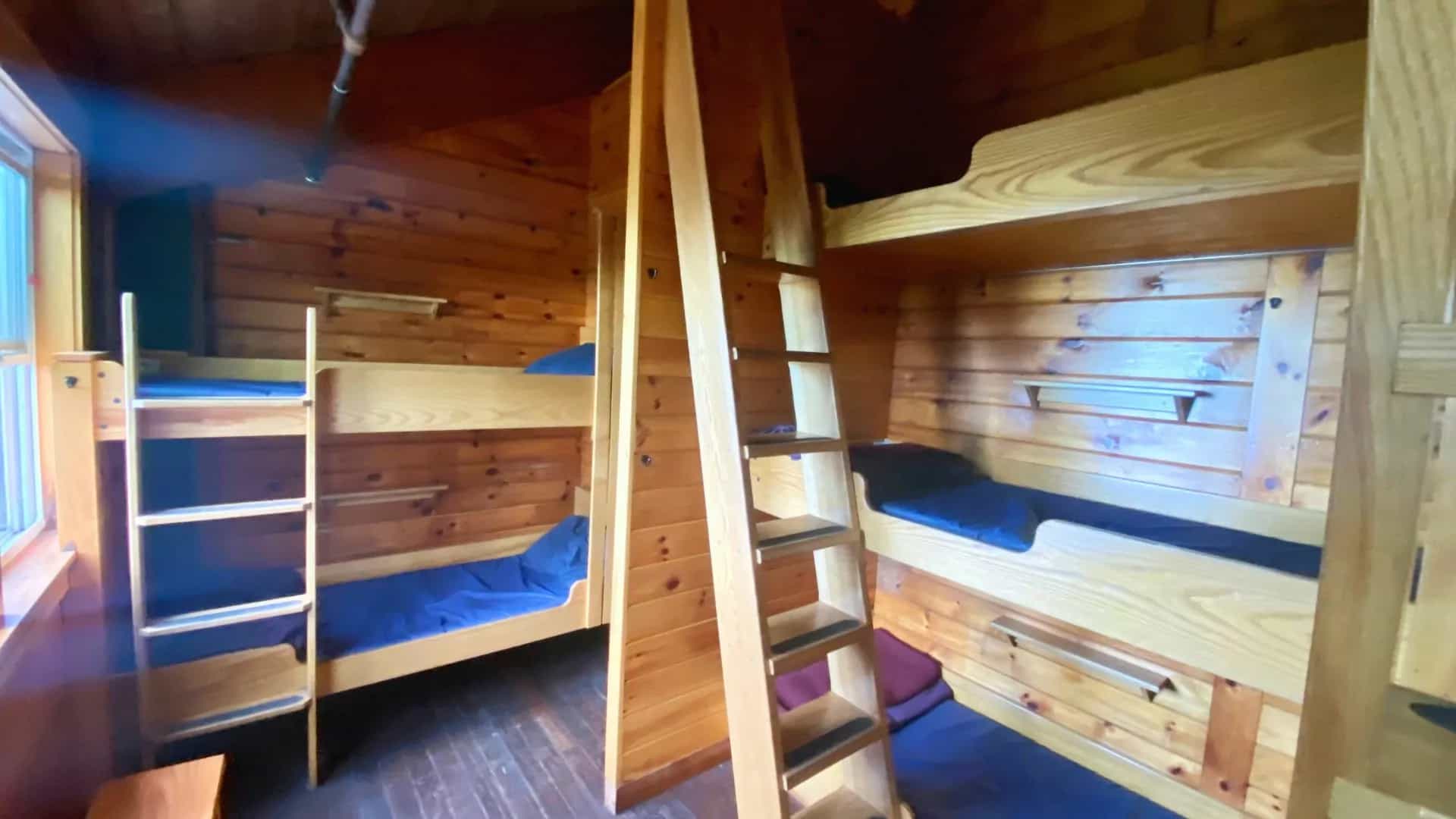 Wooden bunk beds with blue mattresses inside a log cabin room, likely Mizpah Spring Hut.