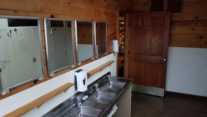 Rustic men's washroom with wood paneling, stainless steel sinks, and mirrors, near Lakes of the Clouds Hut.