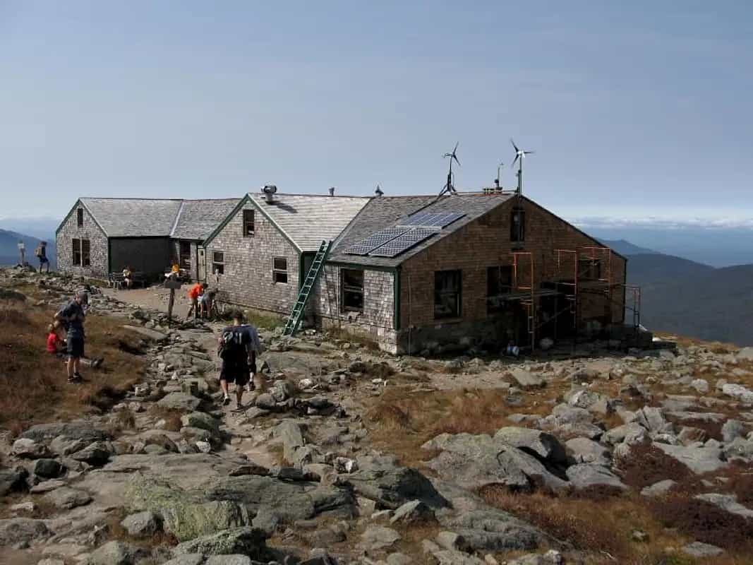 Lakes of the Clouds Hut with solar panels and wind turbines on rocky alpine terrain with hikers.