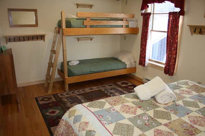Cabin bedroom with wooden bunk beds, patchwork quilt, and bear-themed rug