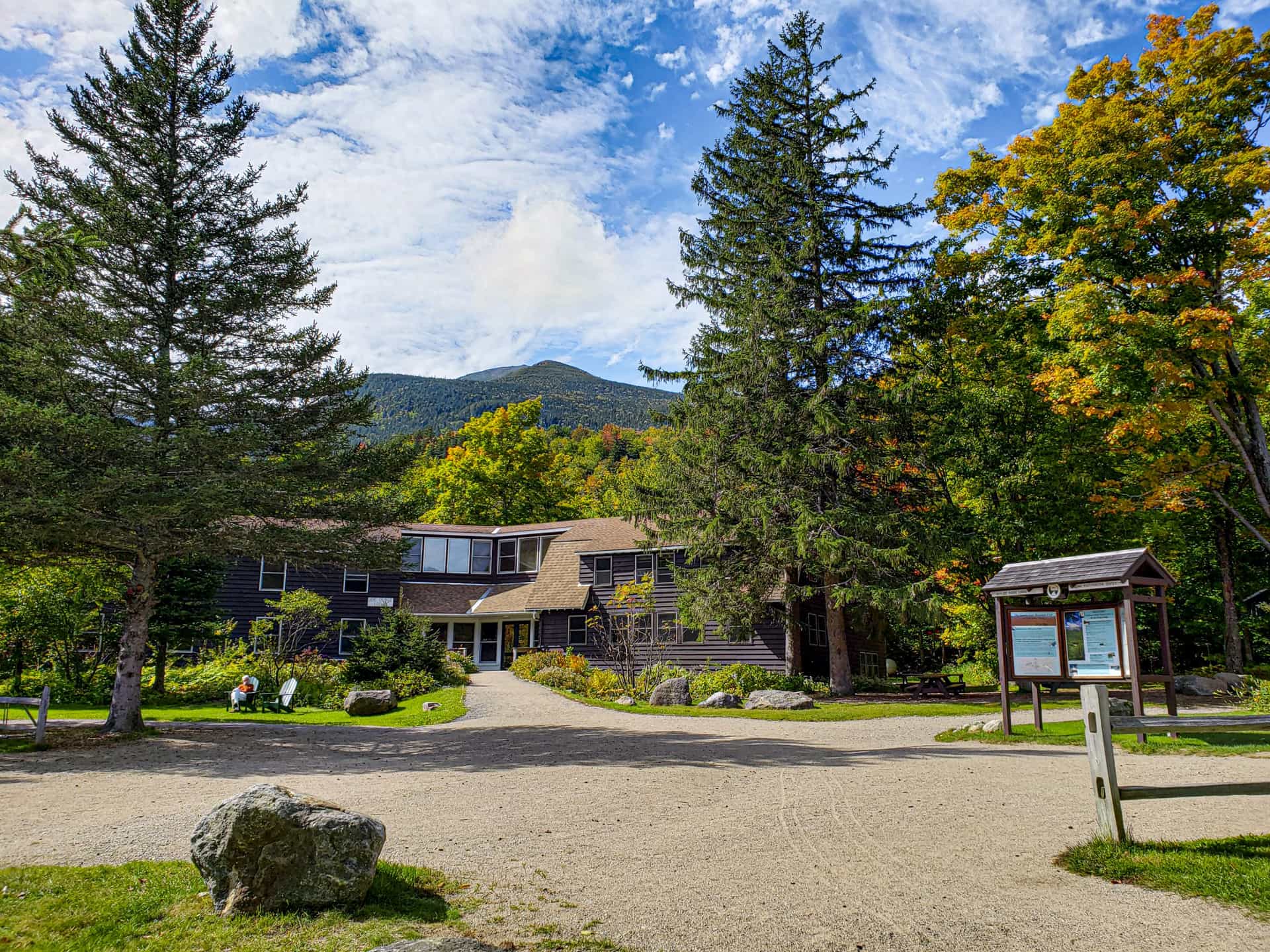 Joe Dodge Lodge with mountain backdrop and autumn foliage under blue, cloudy sky.