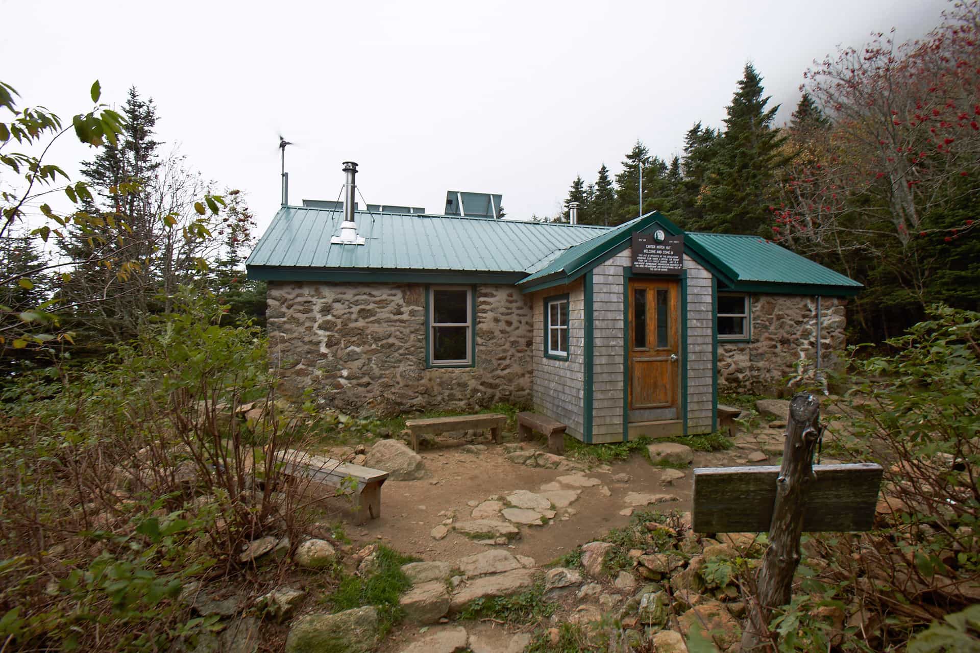 Carter Notch Hut with stone walls and green metal roof surrounded by autumn foliage and evergreen trees.