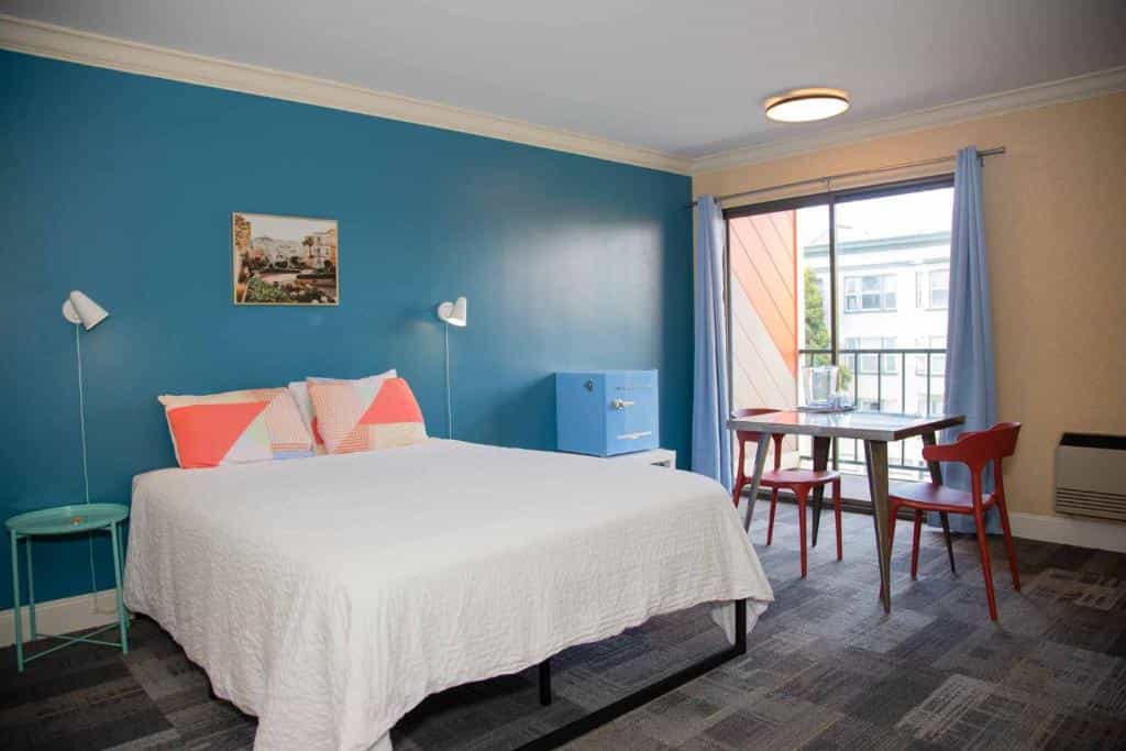 Bedroom with white bed, blue accent wall, and sliding door to balcony in Samesun San Francisco.
