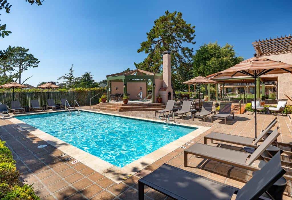 Outdoor swimming pool area with lounge chairs, umbrellas, and a covered spa area at Half-Moon Bay Lodge.