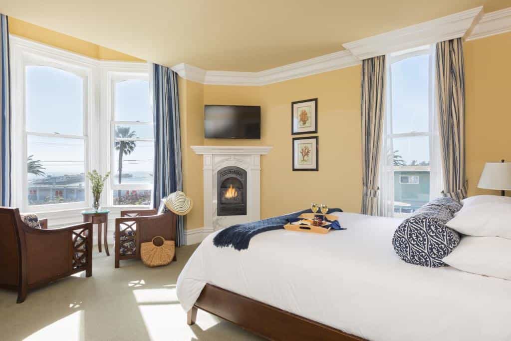 Hotel room with a king bed, fireplace, and large windows overlooking the ocean.