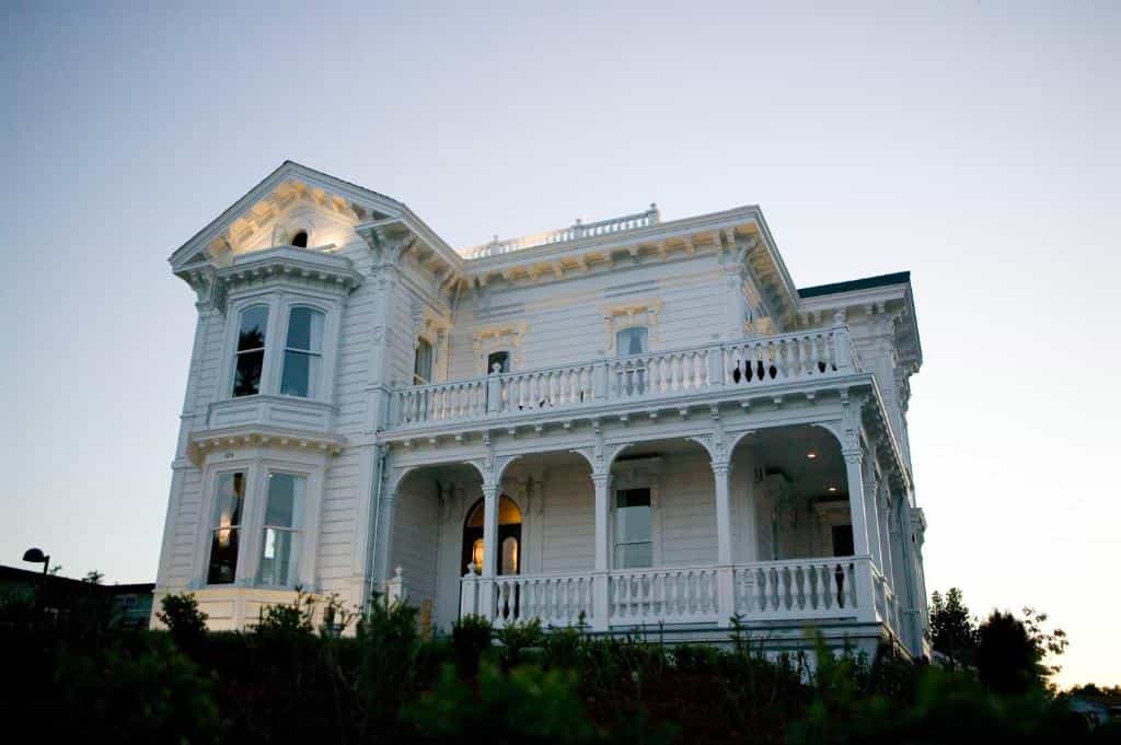 Victorian-style white house with a wrap-around porch and ornate architectural details.