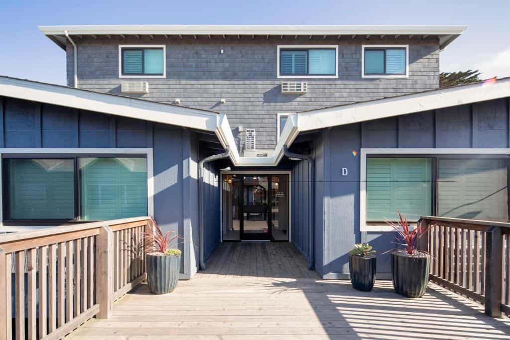 Blue wooden building with a wooden deck entrance and potted plants.