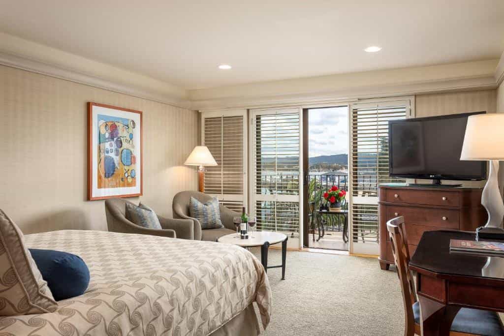 Hotel room with a bed, seating area, and balcony overlooking a harbor.