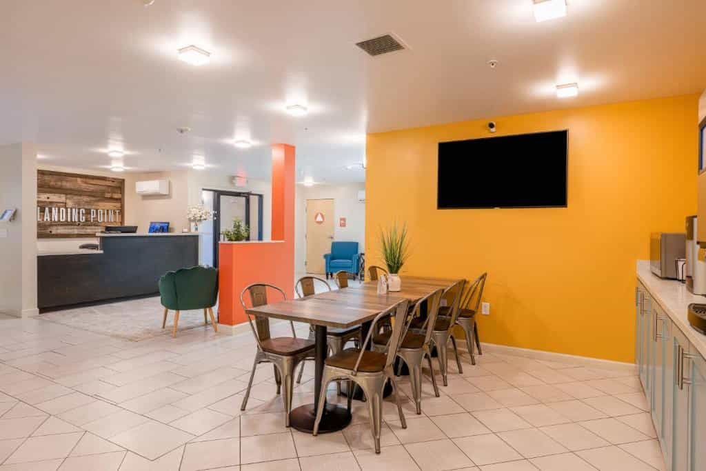 Hotel lobby with dining table, reception desk, and orange accent wall.