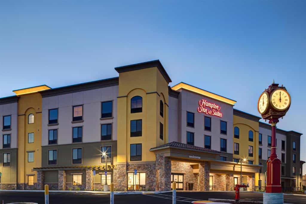 Hampton Inn & Suites hotel building exterior with a decorative street clock at dusk.