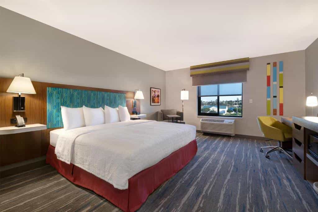 Hotel room with a king bed, desk, armchair, and window view.