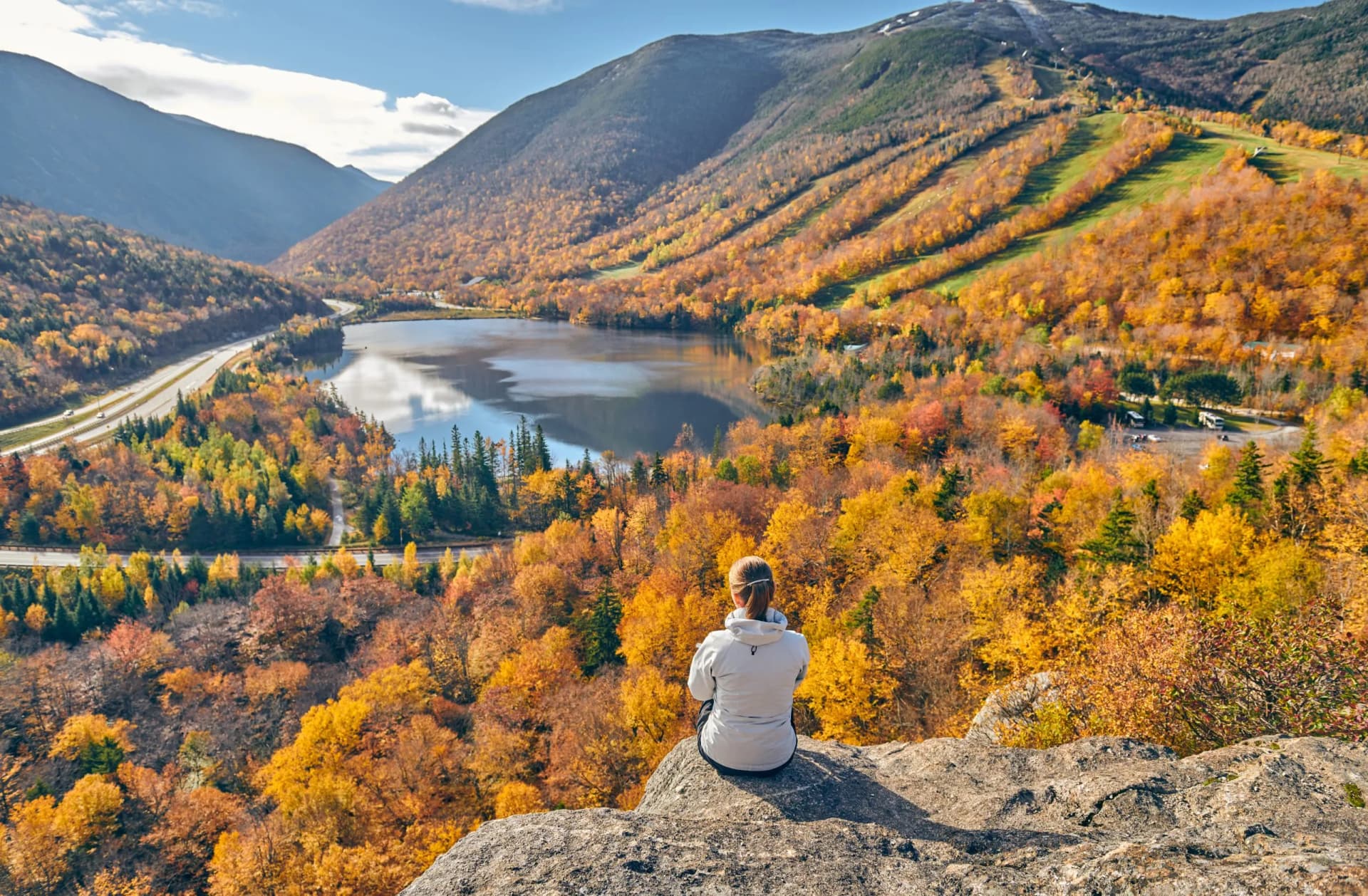 Woman overlooking Franconia Notch State Park autumn foliage, lake, and mountains.