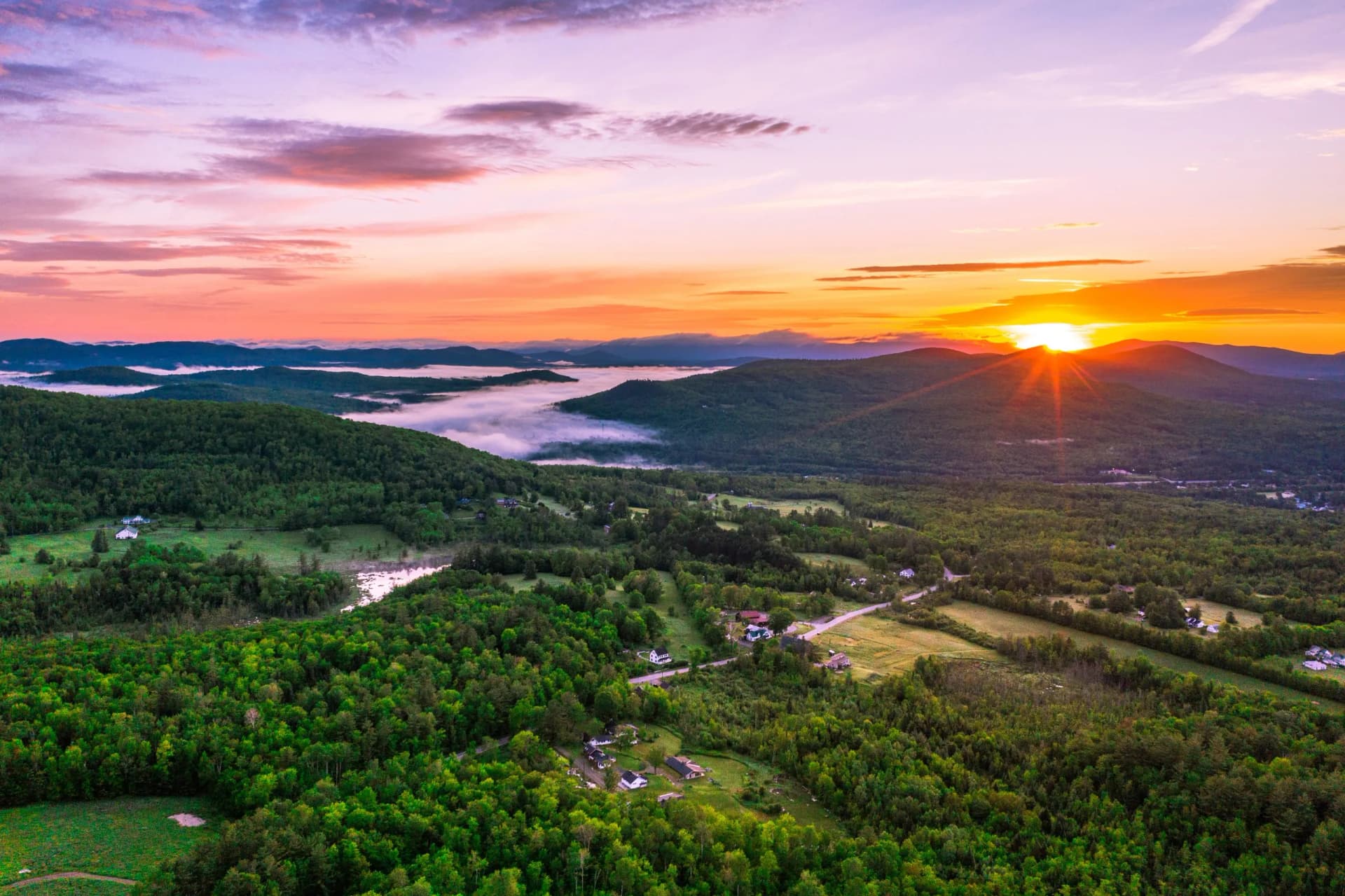 Sunrise over green mountains with fog in valleys and scattered houses.