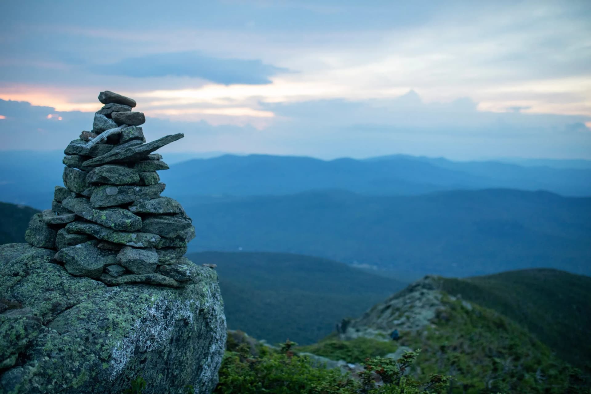 Stone cairn on rocky summit overlooking layered blue mountains at dusk, Mt Adams.