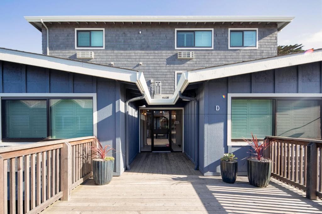 Blue wooden building with a wooden deck entrance and potted plants.