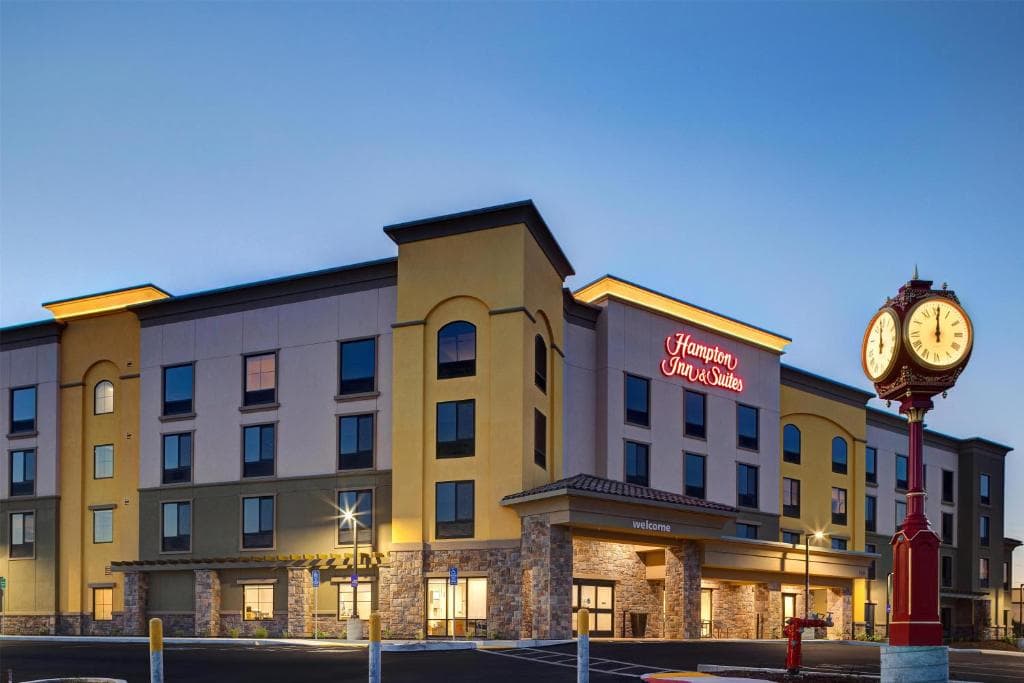 Hampton Inn & Suites hotel building exterior with a decorative street clock at dusk.
