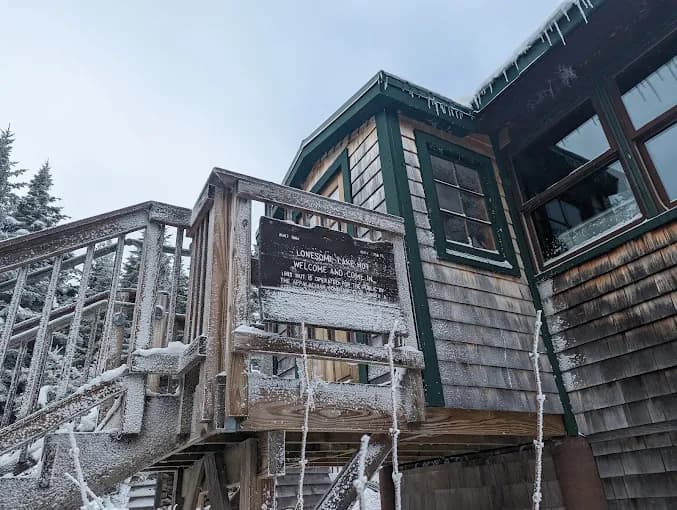 Snow-covered wooden cabin with stairs and frost on railings during winter
