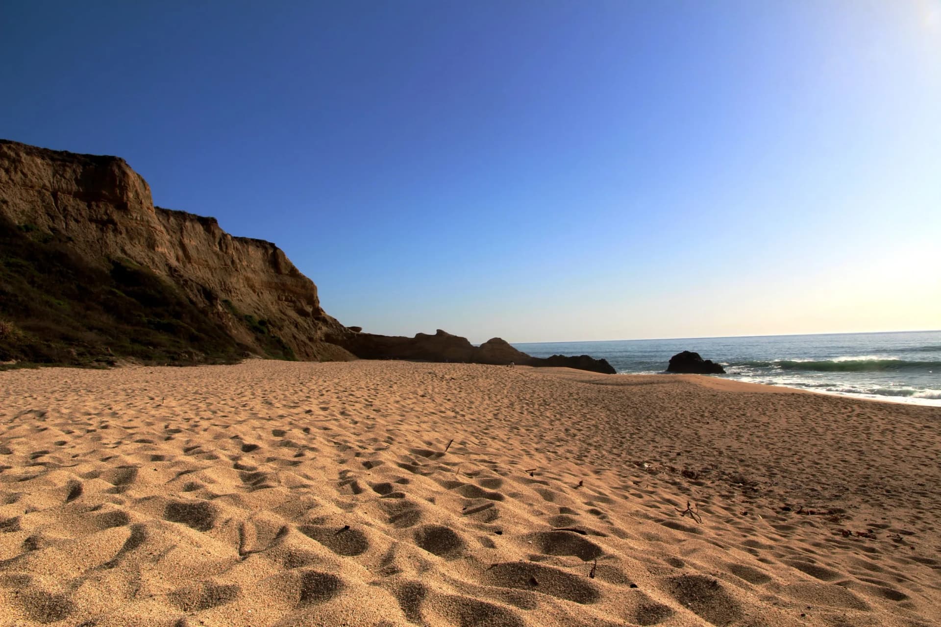 Sandy beach with footprints leading to ocean waves beneath tall coastal bluffs in Half Moon Bay.