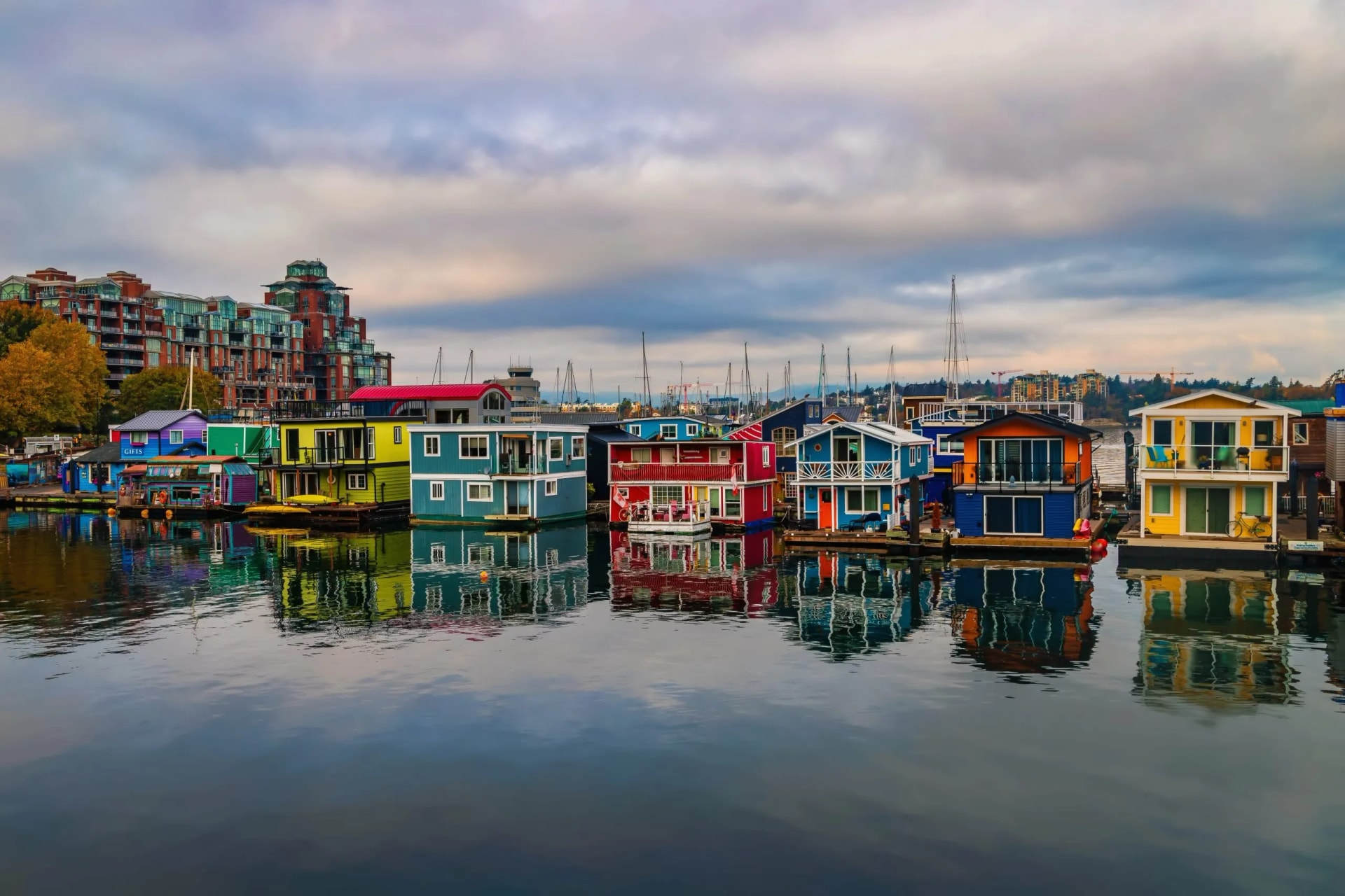 Colorful houseboats docked on water with reflections under a cloudy sky at Fisherman's Wharf Park.