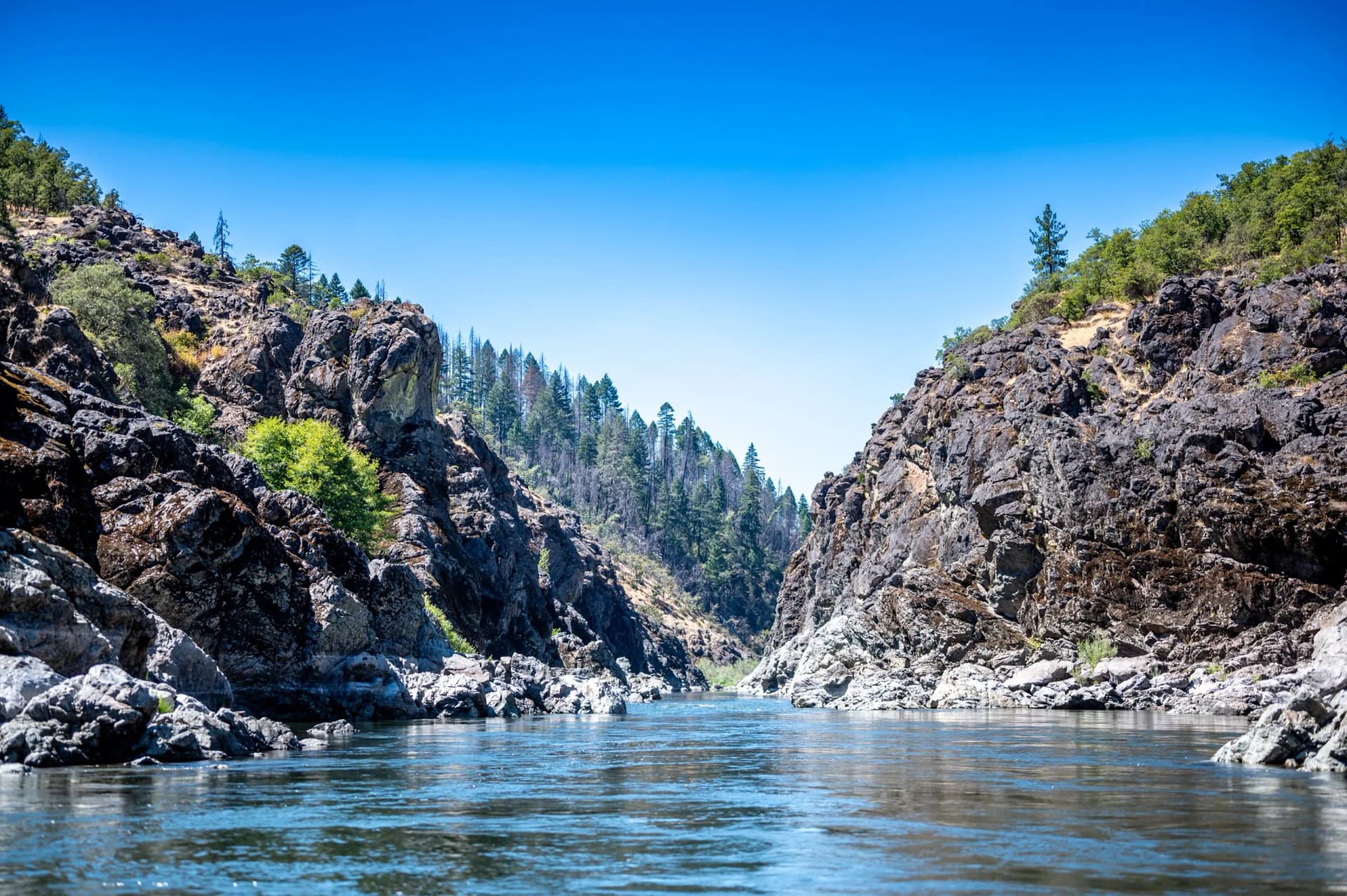 River flowing through Hellgate Canyon on the Rogue River with steep, rocky canyon walls and clear blue sky.