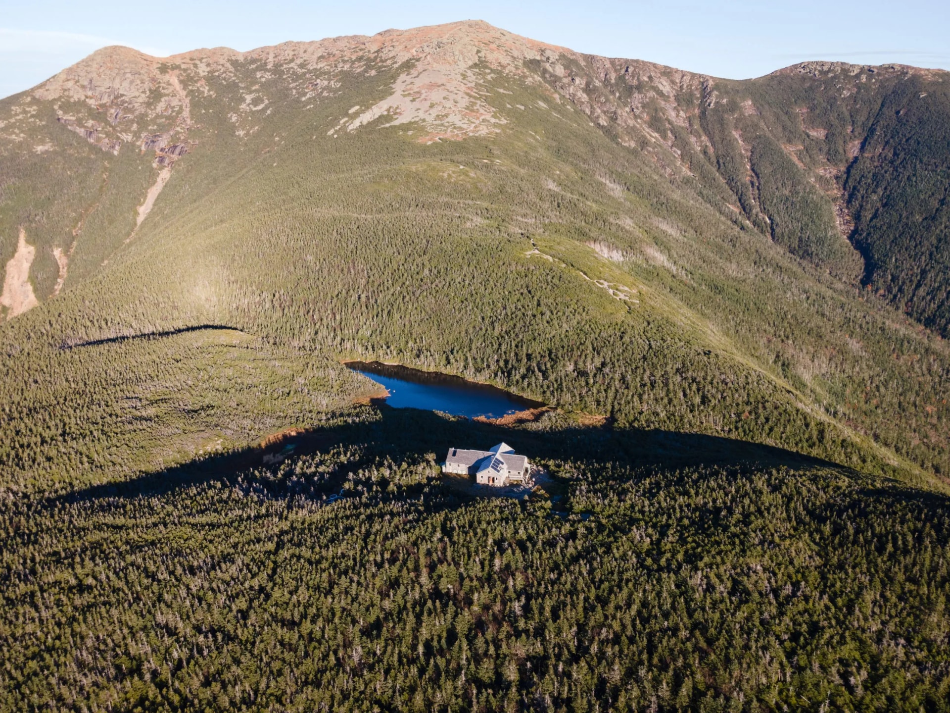 Greenleaf Mountain Hut below summit of Mount Lafayette in White Mountains, New Hampshire, with small lake.