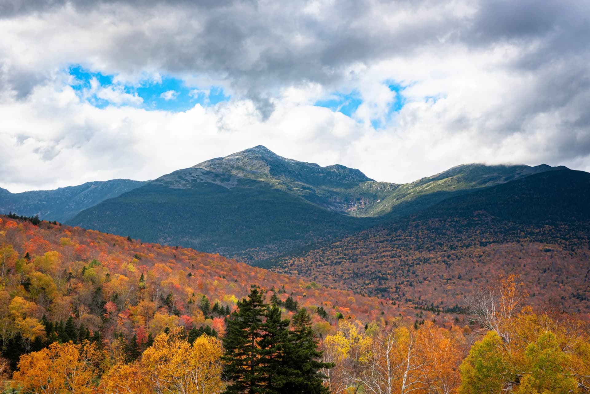 Mount Jefferson and Mount Adams in the White Mountains with vibrant autumn foliage under a cloudy sky.