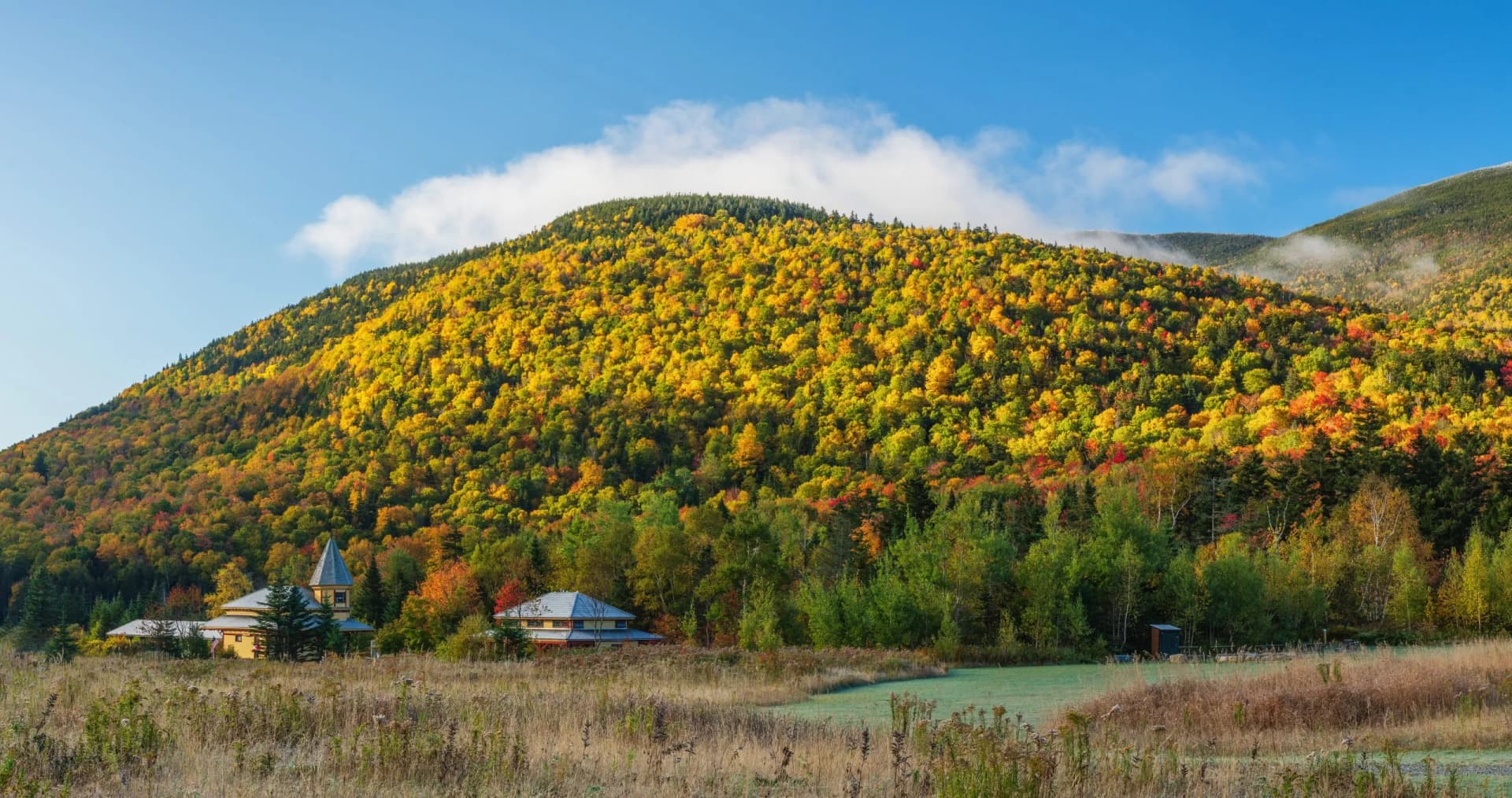 Autumn view of Crawford Notch Station at the AMC Highland Center with yellow foliage on mountains.