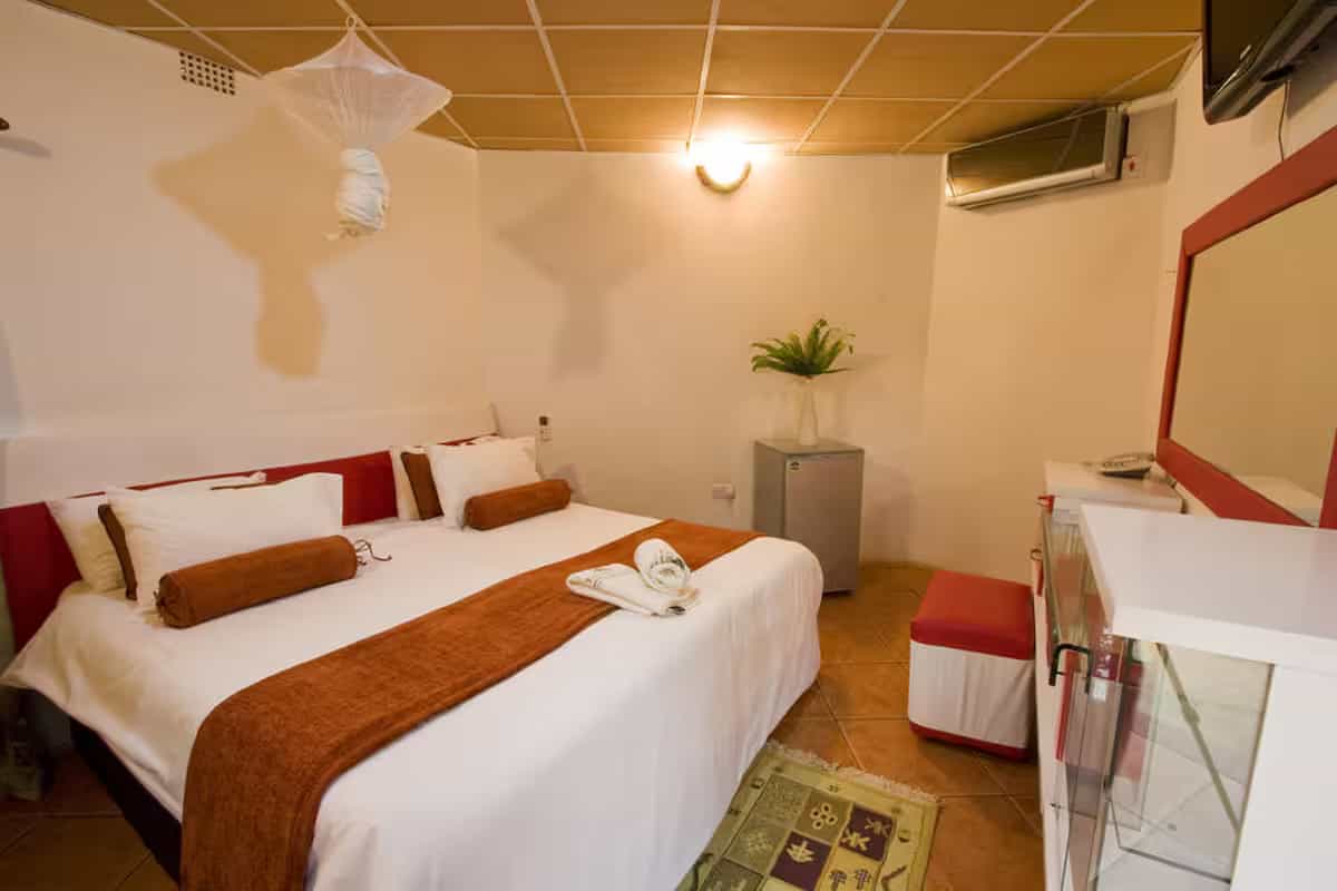 Hotel room with a large bed, white linens, brown runner, mosquito net, and tiled flooring.