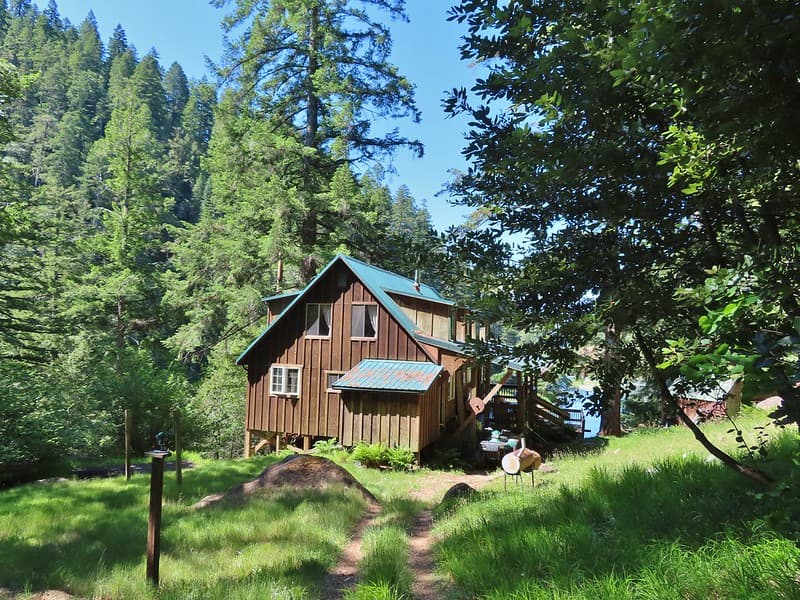 Wooden lodge with green roof nestled in dense forest near water, Clay Hill Lodge